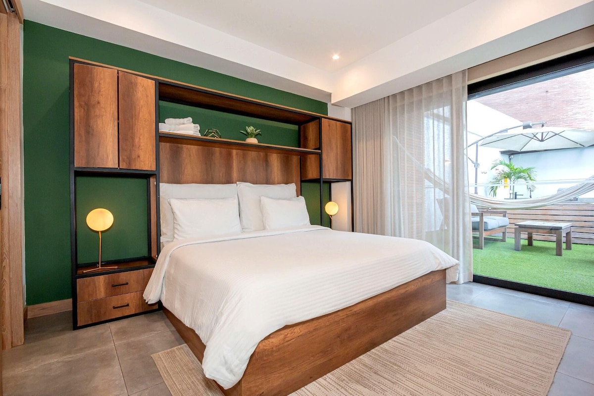 A modern bedroom with a large bed, wooden headboard, and a view of the outdoor area.