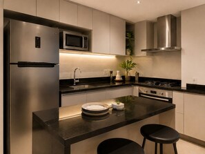 A modern kitchen with stainless steel appliances, a black countertop, and a bar area with stools. - Fully equipped apartment with balcony, pool, and gym. (Barueri)