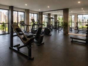 A gym with exercise equipment, large windows, and a city view. - Fully equipped apartment with balcony, pool, and gym. (Barueri)
