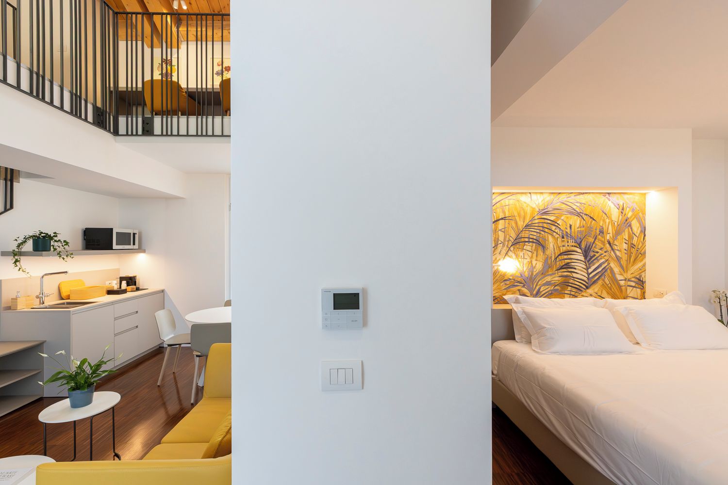 Quarto de hotel moderno com uma cama, termostato fixado na parede e área de cozinha com micro-ondas.