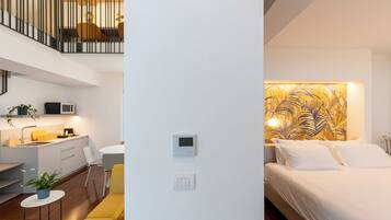 Quarto de hotel moderno com uma cama, termostato fixado na parede e área de cozinha com micro-ondas.