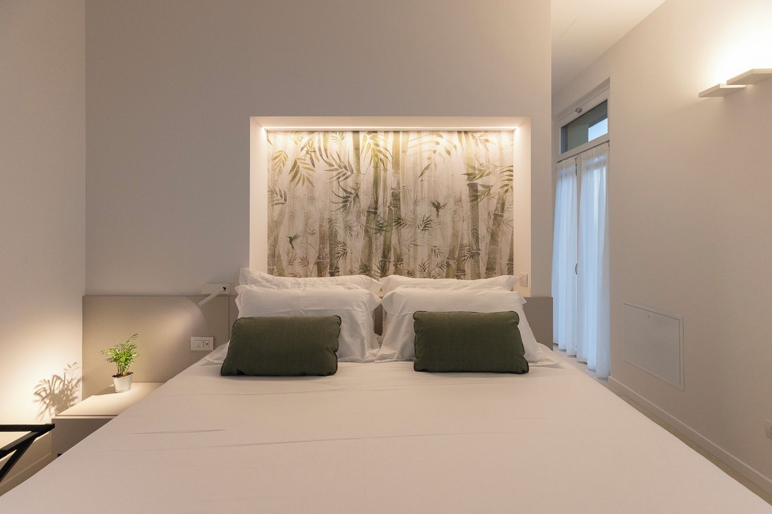 A modern bedroom with a bed, two pillows, a wall-mounted light, and a window with curtains.