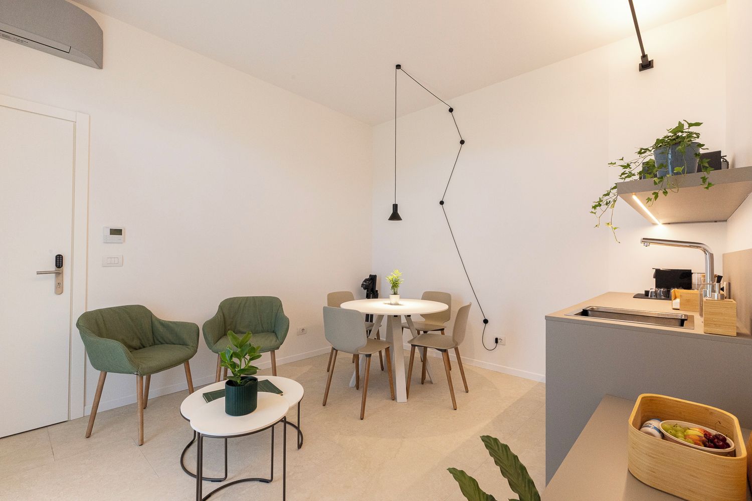 Cuina moderna amb un sollluc incorporat, zona de menjador amb taula rodona i cadirees, i un petit espai d'estar amb dues butaques i una taula auxiliar.