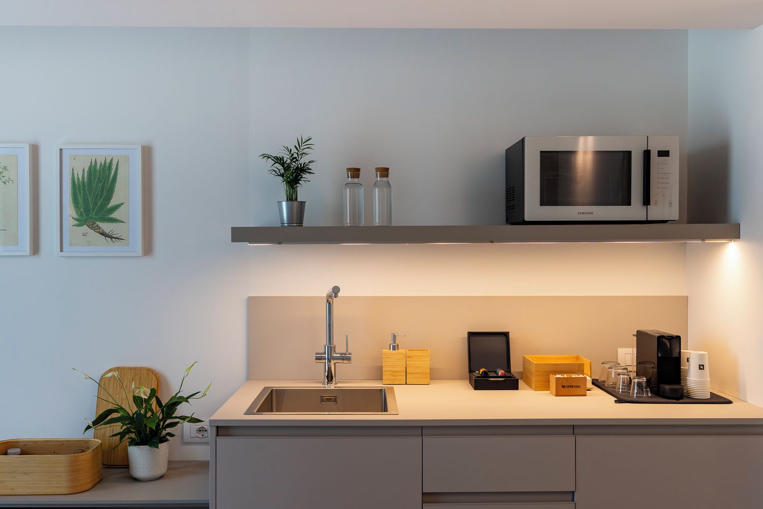 Una cocina moderna con un lavamanos integrado, microondas de acero inoxidable y una estantería con objetos decorativos.