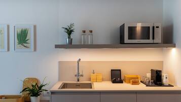 Una cocina moderna con un lavamanos integrado, microondas de acero inoxidable y una estantería con objetos decorativos.