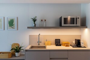 A modern kitchen with a built-in sink, stainless steel microwave, and a shelf with decorative items. - Grow Green (Caponago)