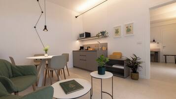 Ein modernes Wohnzimmer mit Essbereich, einer Couch, einem kleinen runden Tisch und einer Küchenzeile.
