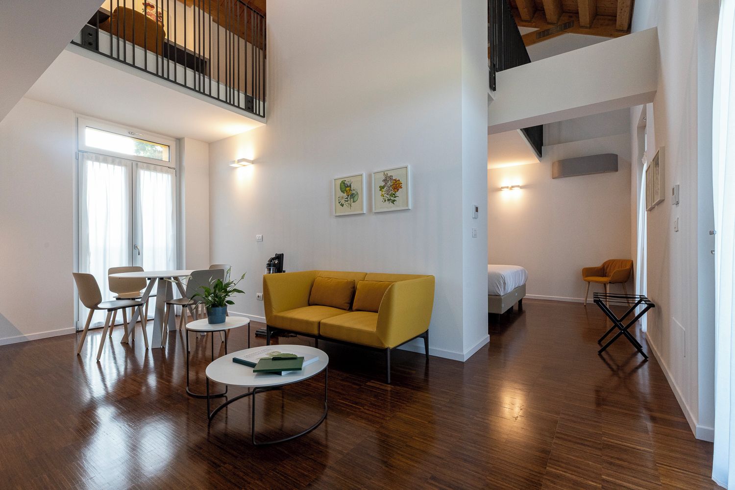 A spacious living area with a yellow sofa, a dining table with chairs, a coffee table, and a staircase leading to an upper level.