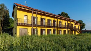 A yellow building with multiple balconies and a red roof, surrounded by greenery. - Grow Green (Caponago)