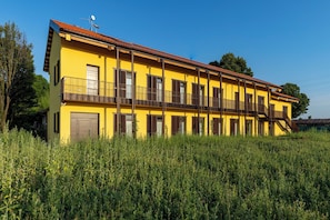 Un edificio amarillo con varios balcones y un techo rojo, rodeado de follaje.