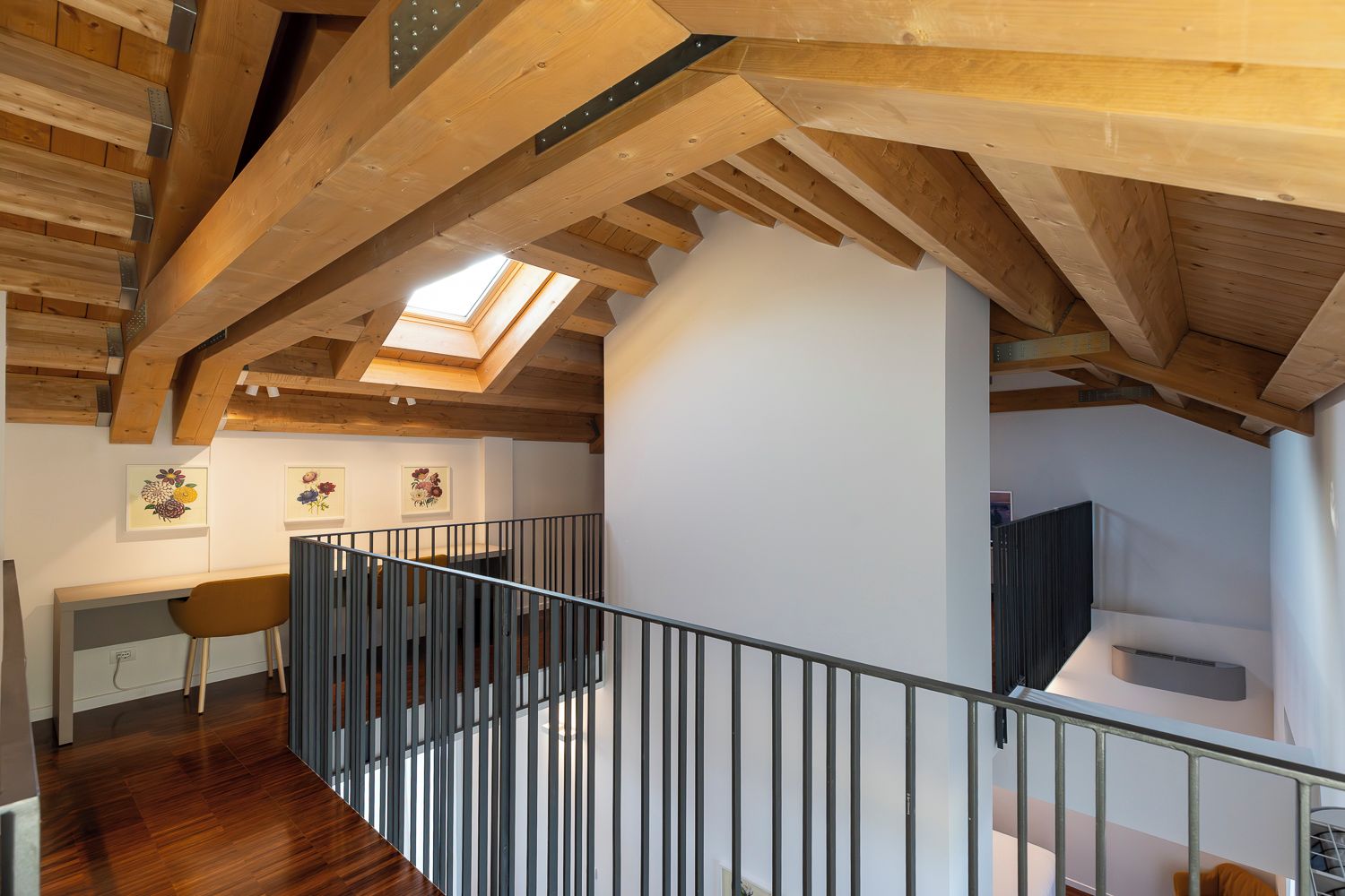 Un interior de madera con tragaluces, una escalera con barandilla metálica y un escritorio con silla.