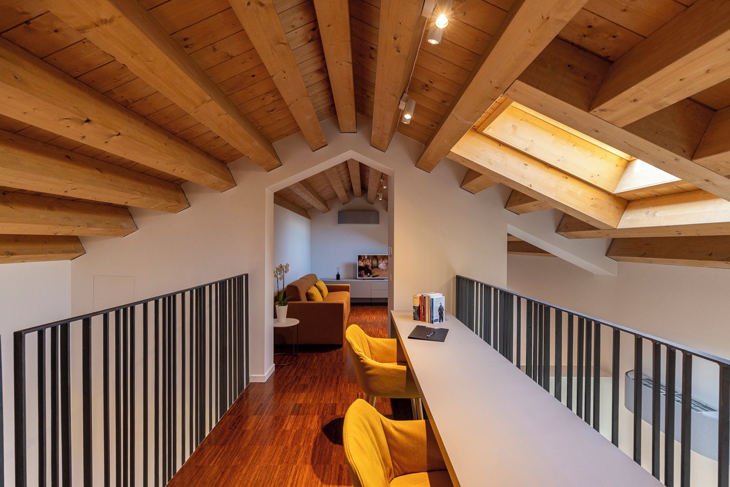 Un loft moderno con vigas de madera a la vista, un comedor con sillas amarillas y una cocina al fondo.