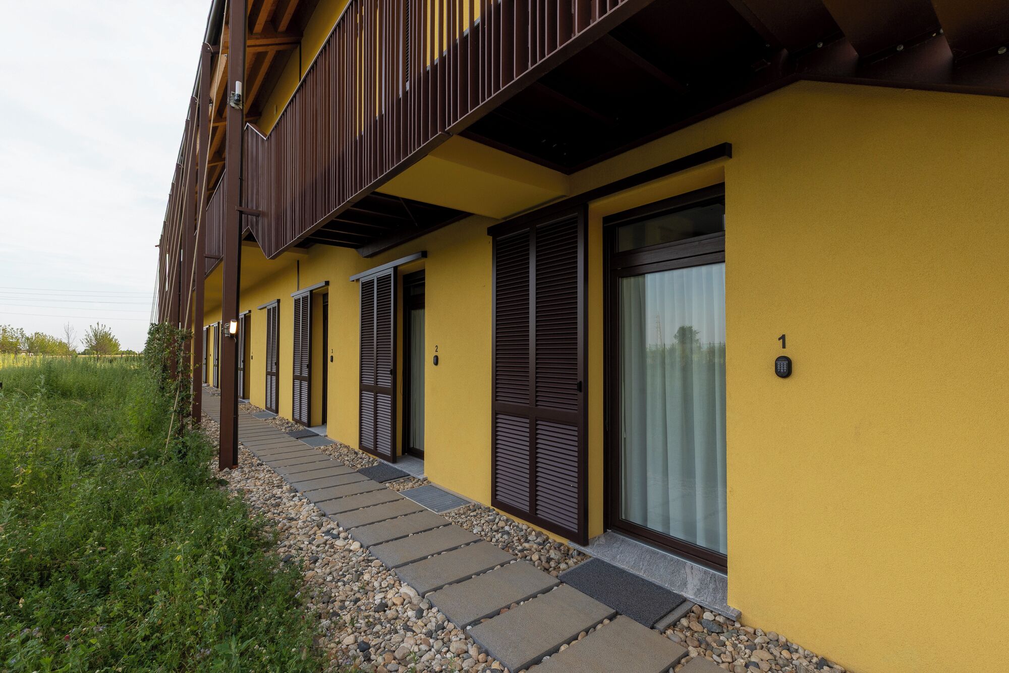 A yellow building with a balcony, numbered doors, and a keypad lock.
