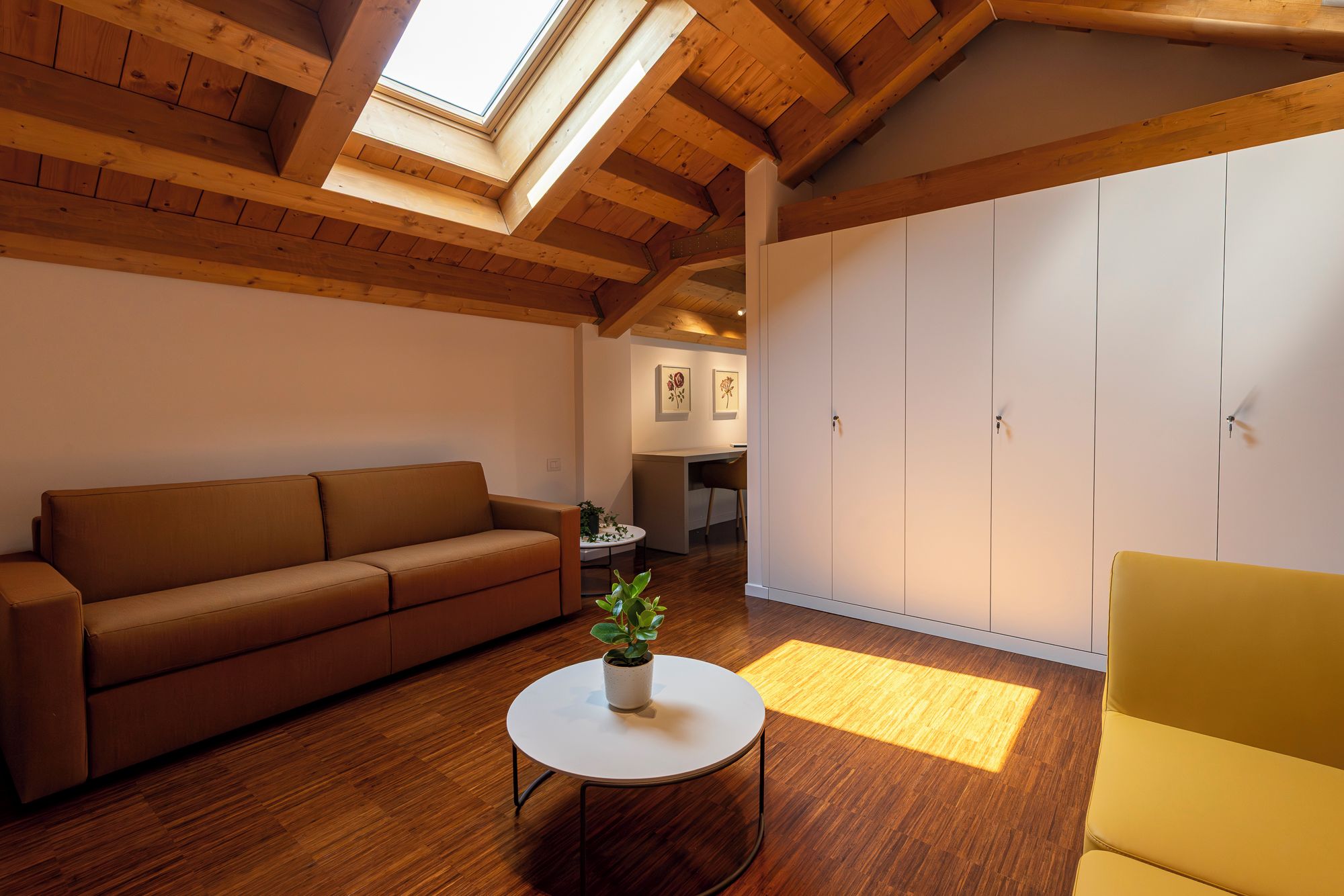 Una sala de estar acogedora con techo de madera, un sofá, una mesita con una planta y un sillón amarillo.