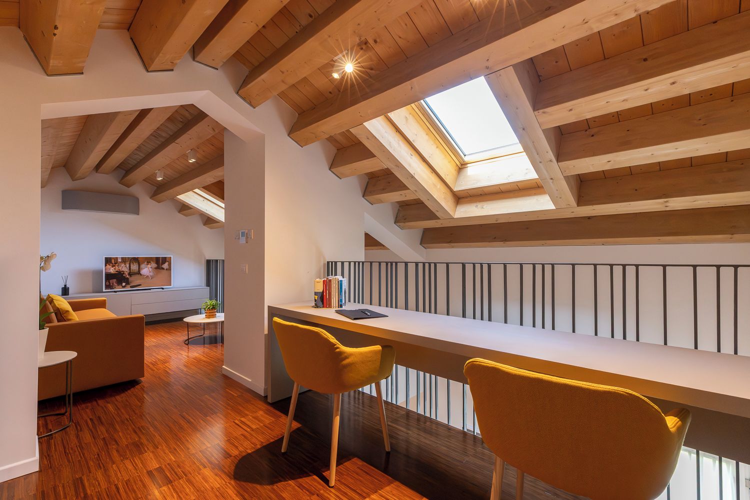 Et moderne loft med skråvægge, træbjælker, et spiseområde med gule stole og et fjernsyn i opholdsstuen.