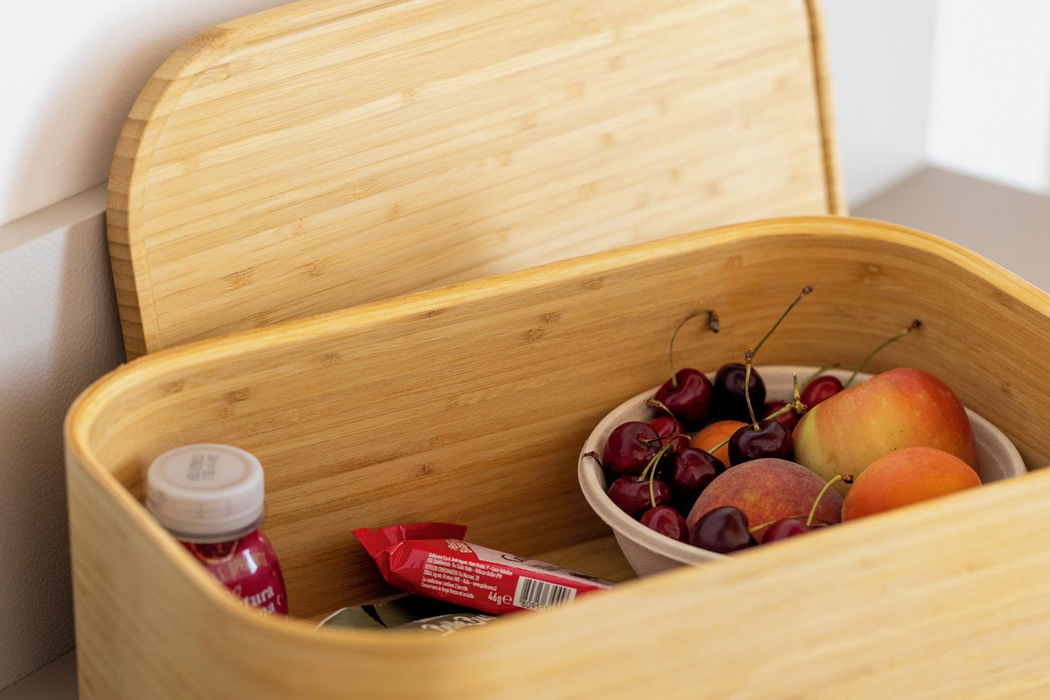 A wooden chest with a hinged lid, containing a bowl of cherries and peaches, and a small bottle.