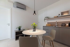 A modern kitchen with a round dining table, chairs, a hanging pendant light, and a built-in microwave. - Grow Green (Caponago)