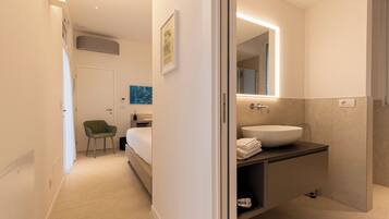 Ett modernt hotellrum med en säng, en grön stol, ett badrum med en stor spegel och ett handfat.