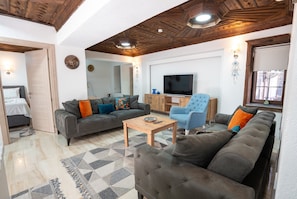 Un salon comprenant un canapé, des fauteuils, une table basse, un téléviseur et un plafond en bois.
