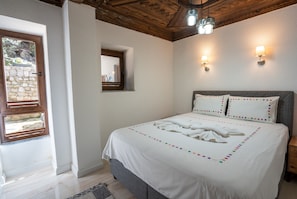 Une chambre à coucher avec un lit, une fenêtre, une lampe fixée au mur et un plafond avec des poutres en bois.