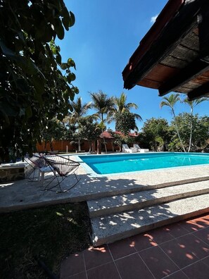 A swimming pool with a tiled deck, surrounded by palm trees and a clear blue sky. - Dianas Home Citlalin (Morelos)
