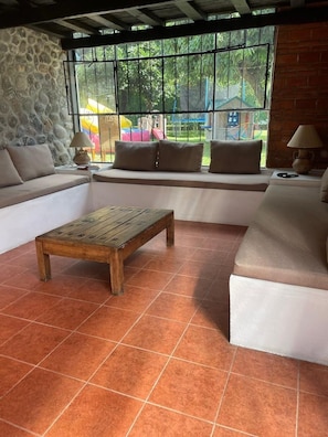 A living room with a stone wall, a large window with a view of a playground, a wooden coffee table, and a sofa set.