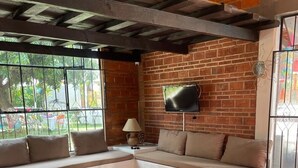 Un espacio de estar acogedor con sofá, una mesa de centro y sillas. Un televisor está fijado a la pared de ladrillo.