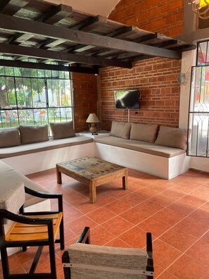 A cozy living area with a sofa, a coffee table, and chairs. A television is mounted on the brick wall. - Dianas Home Citlalin (Morelos)