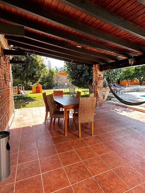 An outdoor patio with a wooden table and wicker chairs, a hammock, and a small playhouse in the background. - Dianas Home Citlalin (Morelos)