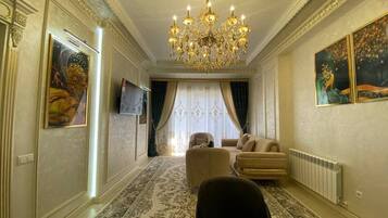 A room with a chandelier, a sofa, a coffee table, and a television.