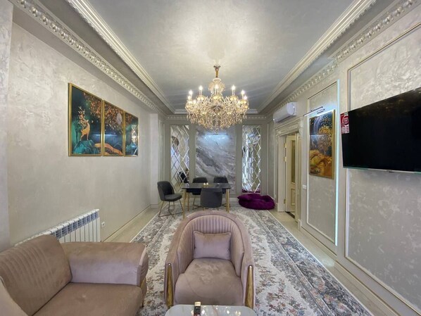 A spacious living room with a chandelier, a dining area, and a television mounted on the wall.