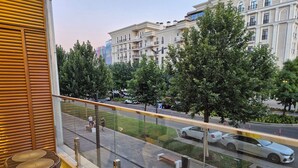 Uma varanda com móveis de vime, vista para uma rua com carros e um edifício com varandas ao fundo.