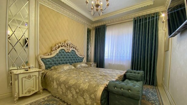 Quarto com uma cama grande, um banco coordenado, uma mesa de cabeceira e um espelho.