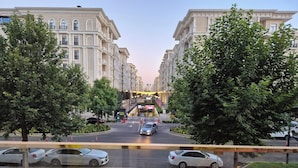 Vista da rua com fileira de edifícios, faixa de pedestres e carros na via.