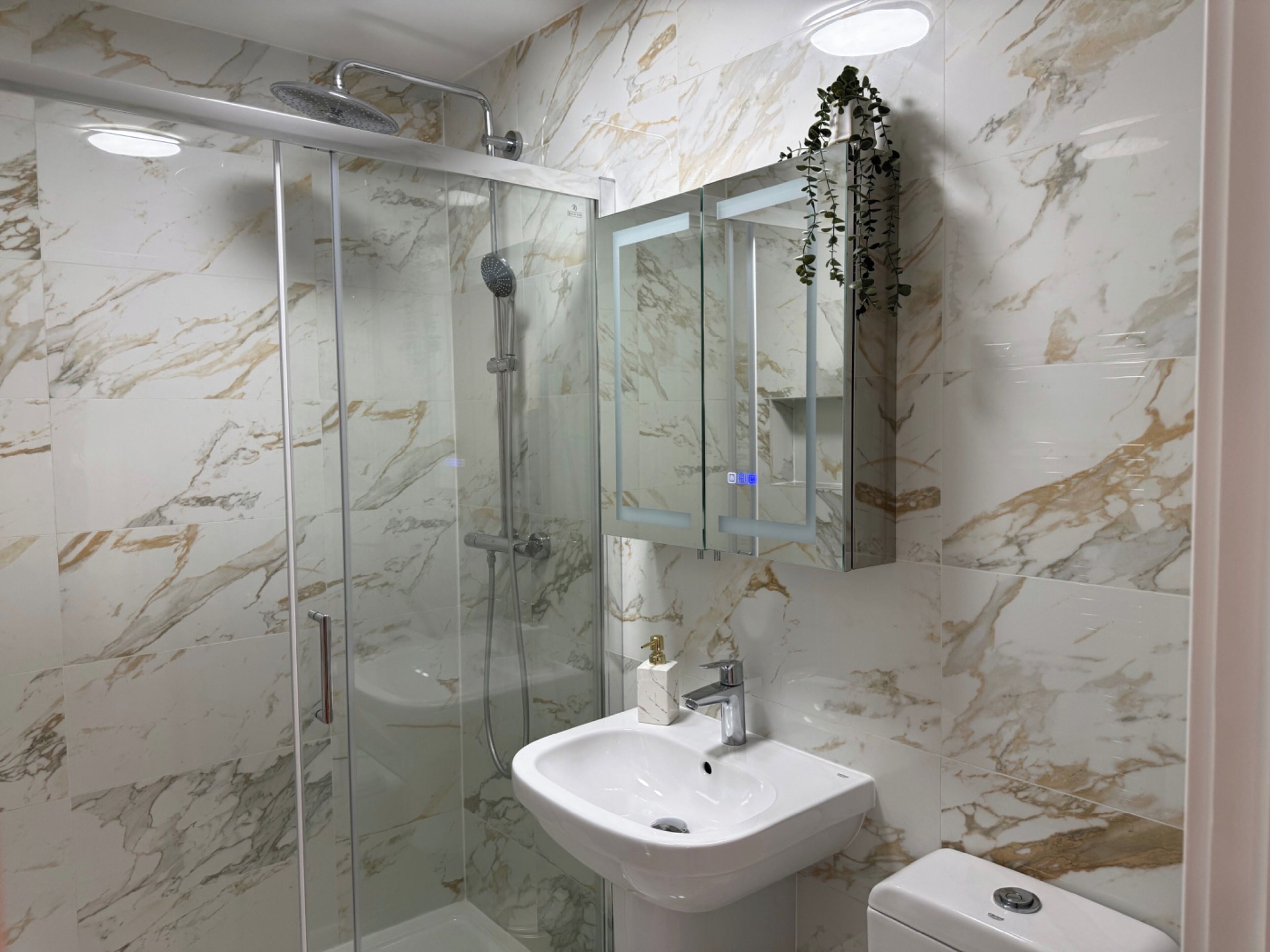 A bathroom with a glass-enclosed shower, a white sink, and a marble-patterned wall.