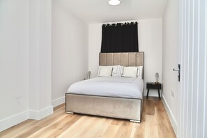 Een slaapkamer met een bed, een nachtkastje, een lamp en een zwart gordijn.