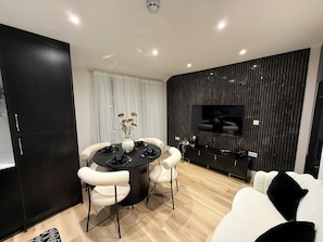 A modern dining area with a round table, white chairs, and a black console table with a flat-screen TV. - Brand New Luxury 4 Bedroom 4 Bathroom Surbiton Flat | 
20min London Waterloo (Surbiton)