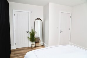 Ein Schlafzimmer mit einem Bett, zwei weißen Türen, einem Spiegel und einem Blumentopf.