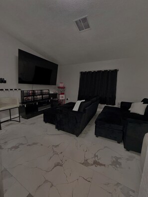 A living room with a flat-screen TV, black sofas, a coffee table, a bookshelf, and a fireplace. - 4BR Home • Private Pool • Themed rooms • Sleeps 14 (Spring Hill)