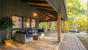 Ett takförsett utomhusområde med sittplatser, en soffa och stolar, ett bubbelbad och en pergola.