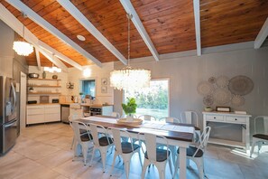 Una cocina moderna con armarios blancos, techo de madera y un comedor con una mesa grande y sillas.
