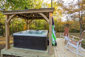 Una vasca idromassaggio sotto un gazebo in legno in una zona boschiva, con sedie a dondolo.