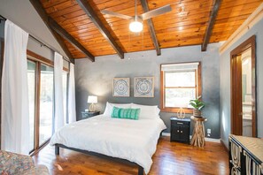 Una camera da letto con soffitto in legno, un letto con biancheria bianca, due lampade a parete e una finestra vista.