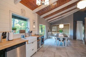 A modern kitchen with a dishwasher, white cabinets, and a wooden countertop. There is a dining area with a table and chairs, and a chandelier hanging above. - Private 3-acre retreat with hot tub and fire pit (Rutherford County)