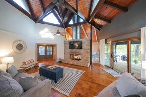 A spacious living room with a stone fireplace, wooden beams, and a large TV. - Private 3-acre retreat with hot tub and fire pit (Rutherford County)