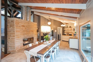 A modern kitchen with a central island, a dining area with a wooden table and white chairs, and a stone fireplace. - Private 3-acre retreat with hot tub and fire pit (Rutherford County)