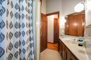Un bagno con tenda da doccia a motivo di foglie, un lavandino bianco con specchio e mobili in legno.