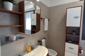 A bathroom with a sink, mirror, towel rack, and shelves. - San Martino Flexrent - Abissinia Real Estate (Riccione)