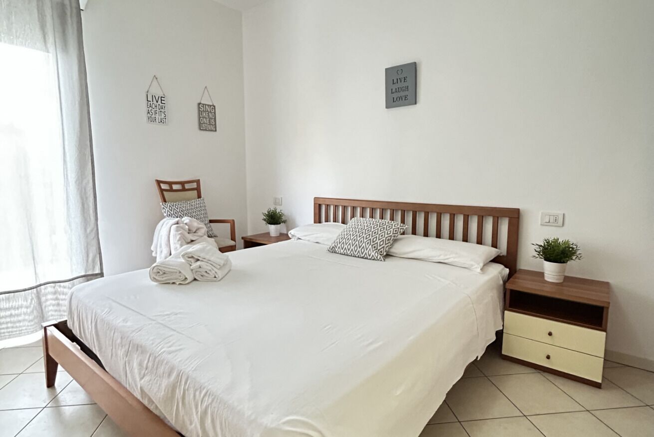 Un letto ordinato con testiera in legno, un comodino con una pianta e decorazioni murali motivazionali.