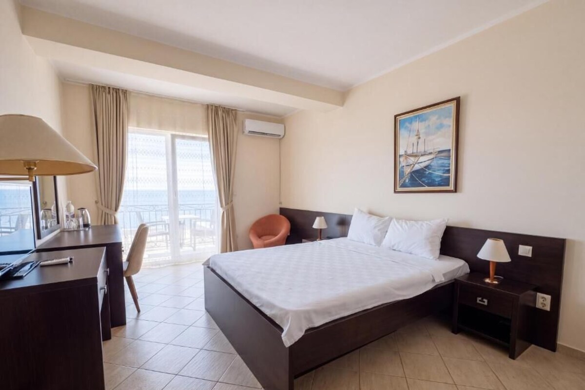 A hotel room with a bed, a desk, a chair, a nightstand, and a painting on the wall.